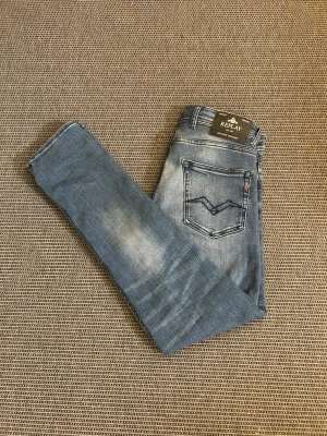 Replay jeans - Säljer ett par blå jeans från Replay med snyggt broderi på bakfickan och klassisk tvättad look. Jeansen har normal midja, raka ben och detaljerade sömmar. Perfekta för dig som gillar stilrena men ändå unika jeans.