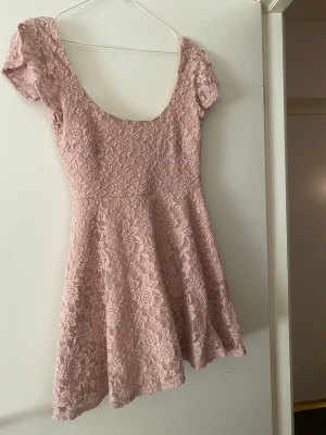 Rosa spetsklänning med kort ärm - Supersöt kort klänning i ljusrosa spets med blommigt mönster. Klänningen har rundad urringning, korta ärmar och är fodrad undertill för extra komfort. Perfekt för dig som gillar romantisk och feminin stil.