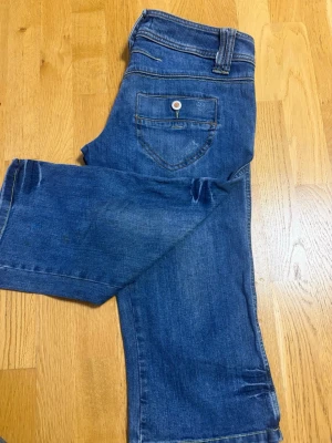 Blå jeans från ICHI med raka ben - Säljer ett par klassiska blå jeans från ICHI med raka ben och snygga kontrastsömmar. Jeansen har fem fickor, bälteshällor och detaljer i metall. Materialet är slitstark denim i bomull. Perfekta för en avslappnad och trendig look.