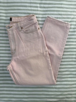 Abercrombie and Fitch mom jeans regular length - Jeans från Abercrombie & Fitch i en ljusrosa nyans. Modellen är "A&F Mom Jeans" med raka ben och en avslappnad passform. Jeansen har klassiska fickor fram och bak samt hällor för bälte. Sömmarna är i en kontrasterande ljus färg.