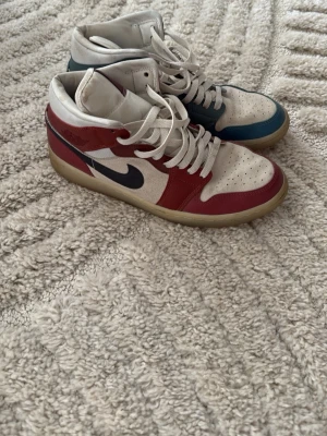 Nike sneakers i rött, blått och vitt - Snygga Nike sneakers med högt skaft i en unik färgkombination av rött, blått och vitt. Skorna har vit bas med röda och blå paneler, klassisk svart swoosh och beige sula. Tillverkade i läder och textil med perforerad tåbox och vita skosnören.