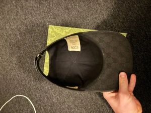 Svart keps från Gucci med GG-mönster - Säljer en svart keps från Gucci med det klassiska GG-monogrammet över hela kepsen. Kepsen har justerbart spänne bak och är tillverkad i ett slitstarkt tygmaterial. Perfekt för dig som vill ha en stilren och exklusiv accessoar. Finns kvitto även 