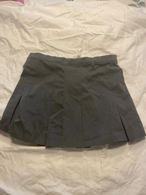 Grå plisserad kortkjol med dragkedja från H&M - Grå skort med plisserad kjoldesign och shorts under. Den har bälteshällor och dragkedja bak för enkel påklädning. Perfekt för dig som vill ha kjol-looken men ändå känna dig bekväm med shorts.