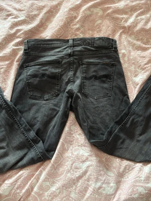Svarta jeans från Nudie Jeans - Säljer ett par svart gråa jeans från Nudie Jeans med klassisk femficksmodell och broderad våg på bakfickorna. Jeansen har normal midja, raka ben och är tillverkade i mjukt denimtyg. Storlek W30 L32 modellen är Lean Dean pris kan diskuteras vid snabb affär 