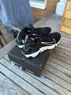 Nike reacts vision  - Svarta Nike Air Max D/MS/X sneakers med vit sula och vit swoosh på sidan. Ovandelen är i mesh för bra andningsförmåga och har svarta skosnören. Snygg detalj med mönstrad hälflik och robust sula för extra komfort.