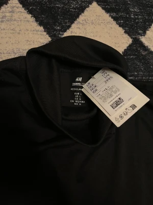 Svart polotopp från H&M, storlek L - Snygg svart polotopp från H&M i storlek L. Tillverkad i mjuk polyester med lång ärm och hög krage. Perfekt för dig som gillar en clean och enkel look med en klassisk twist. Passar till allt och är superenkel att styla.ORDINARIE PRIS:180kr