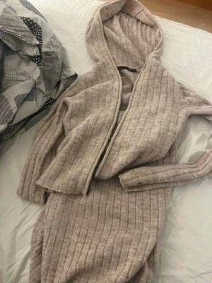 Beige ribbat loungewear-set med hoodie - Mysigt loungewear-set i beige ribbstickat material. Setet består av en långärmad hoodie med luva och matchande byxor. Perfekt för chill hemma eller när du vill vara extra bekväm. Mjukt och stretchigt tyg för maximal komfort.