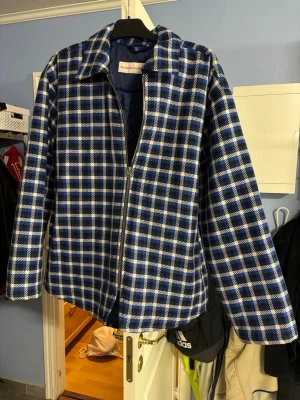 Stockholm surfboard club jacka - Snygg cardiganjacka i blått och vitt rutmönster från Stockholm (Surfboard) Club. Jackan har dragkedja framtill, klassisk krage och quiltat foder för extra komfort. Perfekt för dig som vill ha en unik och trendig look. Nypris 5400