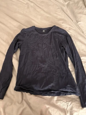 Mörkblå långärmad topp från Cubus - En enkel och stilren mörkblå långärmad topp från Cubus. Tillverkad i mjuk bomull med rund halsringning och normal passform. Perfekt att matcha med jeans eller kjol för en clean look.