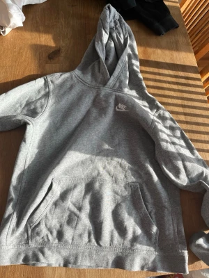 Grå hoodie från Nike med huva - Snygg grå hoodie från Nike med klassisk logga på bröstet. Hoodien har en stor känguruficka framtill och en skön huva. Tillverkad i mjukt sweatshirtmaterial som passar perfekt till vardagslooken. Enkel och stilren design som funkar till det mesta. Går att diskutera pris. Inte använt så mycket 