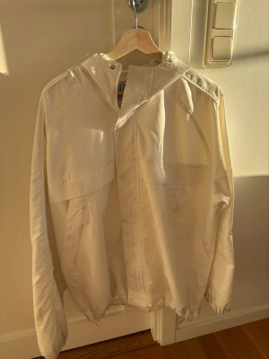 Vit skidjacka från harlautapparel , S - Snygg vit vindjacka från harlautapparel med dragkedja framtill och huva. Jackan har en clean look med diskreta sömmar och justerbar nederkant. Perfekt för dig som vill ha en stilren och enkel jacka till vardags. Materialet känns lätt och smidigt. Lite fläckar här och där