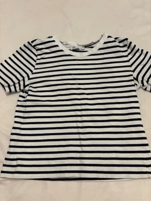 Randig t-shirt från Zara - Säljer en klassisk vit och svart randig t-shirt från Zara. T-shirten har korta ärmar, rund halsringning och är gjord i mjuk bomull. Perfekt för en enkel och stilren look.