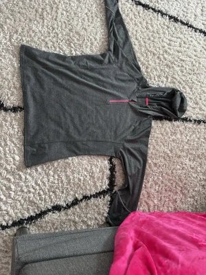 Mörkgrå hoodie med rosa dragkedja - Snygg mörkgrå hoodie från Crivit med halv dragkedja i rosa och matchande rosa kant på insidan av huvan. Tillverkad i mjukt och stretchigt material, perfekt för chill eller träning. Klassisk passform och lång ärm. Kan inte se vilken storlek men det är stor för mig så skulle säga M-L? Aldrig använd men köpte den på second hand så vet inte hur mycket förra ägaren använde den?