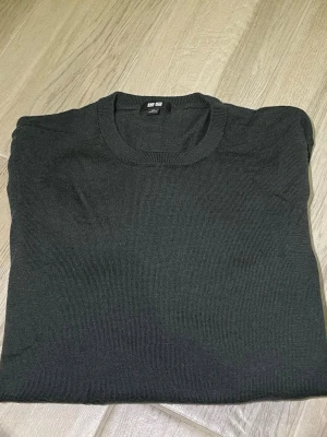 Mörkgrön stickad tröja från Uniqlo - En enkel och stilren mörkgrön stickad tröja från Uniqlo. Tröjan har rund halsringning, långa ärmar och ribbade muddar vid ärmslut och nederkant. Perfekt basplagg för lager på lager och funkar till det mesta.