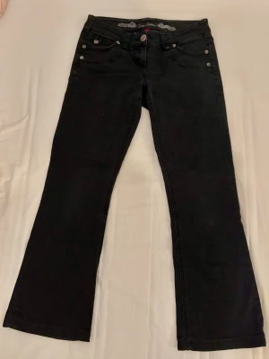Svarta River Island jeans - Svarta utsvängda jeans med låg midja från River Island i bra skick. OBS har sytt upp jeansen så håll koll på innerbenslängden. MIDJEMÅTT: 39cm INNERBENSLÄNGD: 68cm