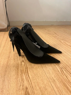Svarta pumps med rosett från hm - Säljer mina helt nya och oanvända svarta pumps från hm med spetsig tå och elegant rosett baktill. Skorna har en smal klack. Perfekta för att lyfta vilken outfit som helst. Storlek 36💞