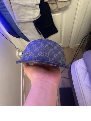 Blå Gucci keps med GG-mönster - Säljer en blå keps från Gucci med det klassiska GG-monogrammet över hela kepsen. Kepsen har böjd skärm och är tillverkad i ett denimliknande material. Snygg och trendig accessoar för dig som gillar exklusiva märken.