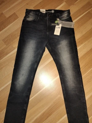 Mörkblå/svarta raka jeans med slitningar (Lab industries) - Snygga mörkblå jeans med raka ben och diskreta slitningar framtill och baktill. Jeansen har klassisk femficksdesign och en något tvättad look som ger en cool vibe. Perfekta för dig som gillar en stilren men trendig look. Aldrig använda.