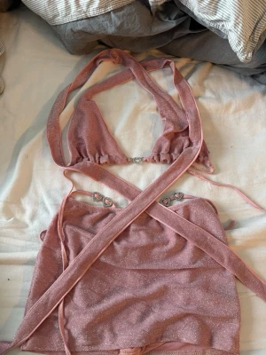 Glittrigt rosa sett med strassdetaljer - Säljer ett glittrigt rosa sett med flera smala axelband och fina strassdetaljer. Settet har en djup urringning och är tillverkad i ett stretchigt material som glittrar. Perfekt för dig som vill sticka ut lite extra.