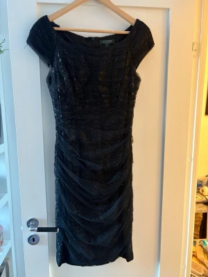Svart glittrig klänning Lauren Ralph Lauren - Svart, glittrig kortklänning från Lauren Ralph med paljettdetaljen. Klänningen har korta ärmar och en elegant, figurnära passform. original pris 3000kr 