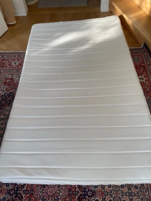  Ny oandvänd Vit madrass i storlek 140/200 - En vit madrass med slät, randig yta och rektangulär form. Passar perfekt för säng eller som extra bädd. Materialet är textil och madrassen är enkel att flytta runt.