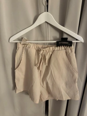 Beiga shorts med snörning - Säljer ett par ljusbeige shorts med snörning i midjan och två sidofickor. Aldrig andvända från SHEIN i storlek M