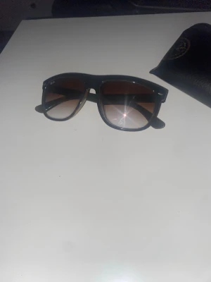 Svarta Ray-Ban solglasögon - Snygga svarta solglasögon från Ray-Ban med klassisk Wayfarer-form och mörktonade glas. Bågarna är i plast och glasen har en brun toning. Medföljer gör ett Ray-Ban fodral i svart skinnimitation.