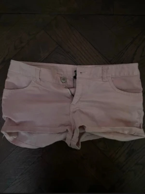 Ljusrosa shorts med uppvik - Säljer ett par ljusrosa shorts med uppvikta benslut och klassisk femficksdesign. Shortsen har bälteshällor och stängs med knapp och dragkedja. Perfekta för varma dagar och ger en avslappnad look. Har en liten missfärgning på knappen men inget som man tänker på! Köpta på hm för längesedan!