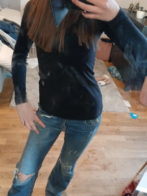 Blå slitna jeans - Säljer ett par blå jeans med slitningar och hål på knäna. Jeansen har raka ben, klassisk femficksmodell och knappgylf. Materialet är denim i bomull och de har en avslappnad passform. Perfekta för en cool och avslappnad stil.