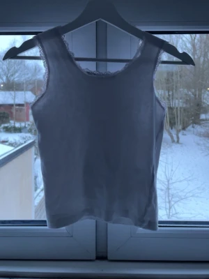 Vit ribbad linnetopp med spets - Säljer en vit ribbad linnetopp från 157 med fina spetsdetaljer runt halsringningen och ärmhålen. Perfekt att styla till jeans eller kjol för en clean och fräsch look. Materialet är mjukt och stretchigt för extra komfort.