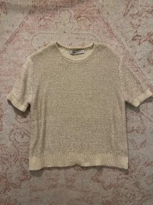Glittrig beige topp från Zara - Snygg beige topp från Zara med korta ärmar och rund hals. Toppen är stickad och har glittriga paljettdetaljer som ger ett extra lyft till outfiten. Perfekt för dig som vill sticka ut lite extra med en enkel men ändå festlig look.