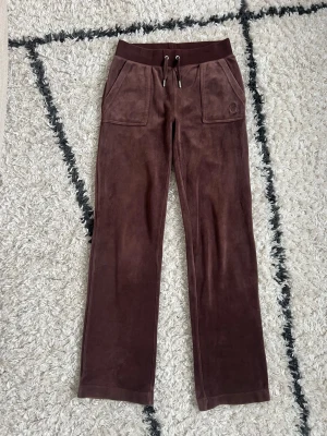 Bruna mjukisbyxor i velour - Mysiga bruna mjukisbyxor från Juicy Couture i velour. Byxorna har raka ben och två stora fickor framtill. Storlek XS. Något slitna längst ner på benen och har en liten fläck, lite noppriga vid resåren 🤎