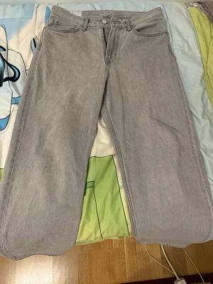 Gråa raka jeans i denim - Säljer ett par gråa jeans med rak passform och klassisk femficksdesign. Jeansen har hög midja och är tillverkade i ett mjukt denimtyg. Perfekta för en avslappnad och trendig look.