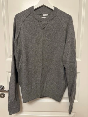 Stickad tröja från Filippa K - Grå stickad tröja från Filippa K. Tröjan har rund halsringning med ribbade muddar och en snygg detalj vid halsen. Perfekt basplagg för en avslappnad och stilren look.