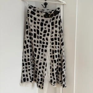 Vit och svart kjol med bälte - Säljer en vit kjol med svart abstrakt mönster och ett snyggt bälte i midjan. Kjolen har en lätt utställd form och är perfekt för dig som gillar en unik och trendig stil. Materialet känns mjukt och luftigt, vilket gör den skön att bära.