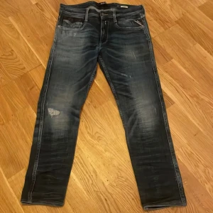 Replay jeans  - Säljer ett par mörkblå jeans från replay med snyggt slitna detaljer och kontrastsömmar. Jeansen har klassisk femficksmodell, raka ben och en tvättad look med ljusare partier. Perfekta för en avslappnad och trendig stil.