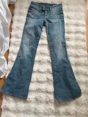 Blå bootcut jeans från Diesel - Säljer ett par blå bootcut jeans från Diesel med dubbla knappar i midjan och coola detaljer på fickorna. Jeansen har en klassisk tvättad look och är tillverkade i slitstarkt denim. Aldrig använda då jag köpte en storlek för liten!! Längden passar mig som är 177❤️