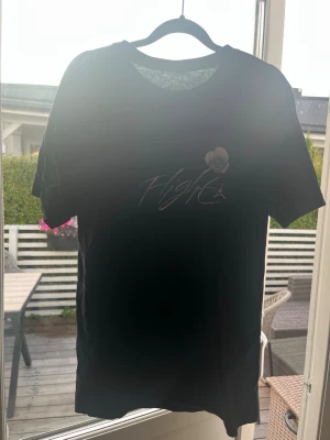 Svart t-shirt Jordan - Svart t-shirt med tryck av en basketspelare och texten 'Flight' på framsidan. Klassisk rund hals och korta ärmar. Perfekt för dig som gillar sportiga och stilrena plagg.