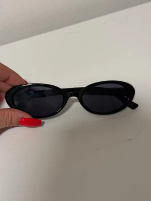 Svarta ovala solglasögon Bik Bok  - Snygga svarta solglasögon med ovala bågar och mörka glas. Klassisk och stilren design som passar till många olika outfits. Bågarna är i plast och har en enkel look utan synligt märke.