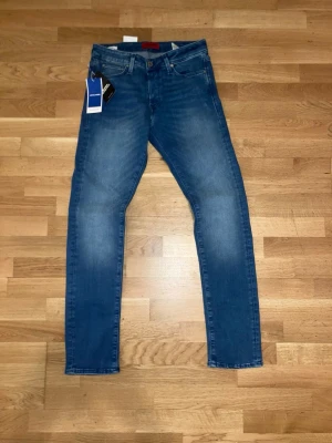 Blå Jack & Jones slim fit jeans - Snygga oanväna blå slim fit jeans från Jack & Jones med tvättade detaljer. Jeansen har normal midja och smala ben, perfekta för en trendig och avslappnad stil. Tillverkade i mjukt denimtyg som ger en bekväm känsla hela dagen.