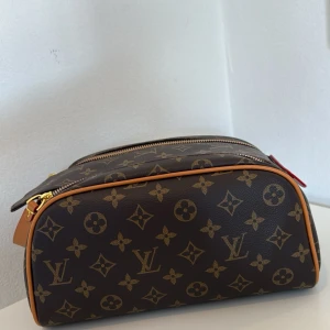 Nyskick trendig och klassisk brun necessär i monogram mönster - Fin necessär i klassiskt brunt monogrammönster med guldiga dragkedjor rymlig stor modell. Den har två dragkedjor upptill och är både praktisk och snygg. Perfekt för att organisera dina essentials.