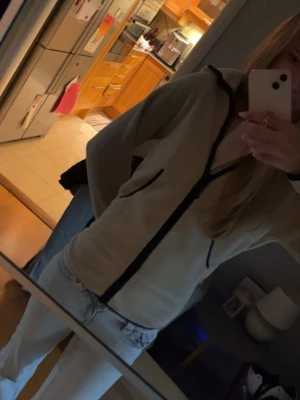 Beige fleecejacka med svarta detaljer - Mysig beige fleecejacka med svarta dragkedjor och kantband. Jackan har hög krage och två fickor framtill. Perfekt för lager-på-lager och chill dagar. Enkel och stilren design som passar till det mesta.