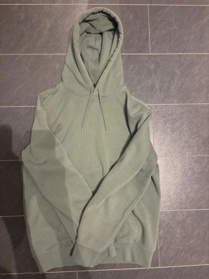 Grön hoodie med huva och ficka - Säljer en stilren hoodie i ljusgrön färg med klassisk huva och dragsnören. Hoodien har en magficka och ribbade muddar vid ärmslut och nederkant. Perfekt för en avslappnad och trendig look.