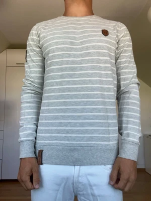 Ljusgrå och vit randig tröja - Randig tröja från Naketano tillverkad i 75% bomull och 25% polyester. Strl S. Inga defekter. Modellen är 178 cm och väger 77 kg. Hör gärna av dig vid frågor!
