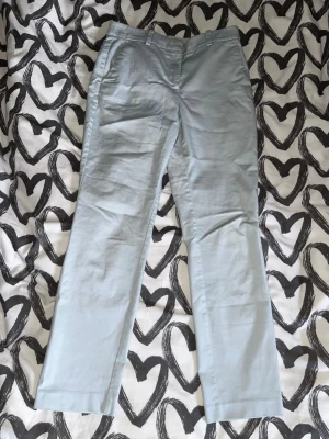 Chinos Kostymbyxor  - Snygga ljusblå chinos med raka ben och klassiska fickor fram. Byxorna har hällor för bälte och stängs med dragkedja och knapp. Perfekta för en clean och stilren look. Materialet känns mjukt och bekvämt, troligen bomull eller bomullsblandning. Knappt använda