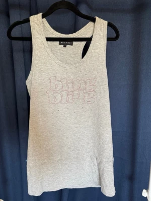 Grå linnetopp med bling från Bik Bok - Säljer en grå ärmlös linnetopp från Bik Bok med texten 'bling bling' broderad framtill och små glittriga detaljer. Perfekt för dig som gillar en chill men ändå lite extra look. Mjuk och skön bomullskänsla.