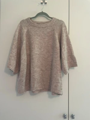 Stickad t-shirt  - Mysig beige stickad tröja med avslappnad passform och halvlånga ärmar. Tröjan har rund halsringning och ribbade kanter vid ärmslut och nederkant. Perfekt för lager på lager och enkel att styla till olika outfits.