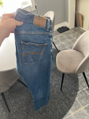 Nudie Jeans - Snygga blå jeans med klassisk femficksdesign och kontrastsömmar på bakfickan. Jeansen har normal midja och raka ben. Tillverkade i ett mjukt denimtyg som ger en avslappnad look. Perfekta för dig som gillar en tidlös och enkel stil. Storleken är 30 30 