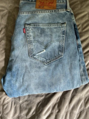 Levi's  jeans med slitningar  - Ljusblå Levi's jeans med klassisk femficksdesign och rakt ben. Jeansen har en snygg tvättad look och en liten slitning på ena bakfickan. Tillverkade i bomull med den ikoniska läderpatchen bak i midjan.