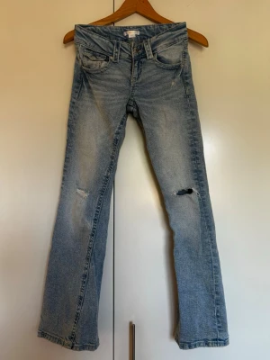 Ljusblå bootcut jeans med slitningar från Gina Tricot storlek 152/ XXS - Säljer ett par ljusblå bootcut jeans med slitningar på båda benen. Jeansen har klassisk femficksdesign, låg midja och är tillverkade i denim. Perfekta för ca 160 lång.